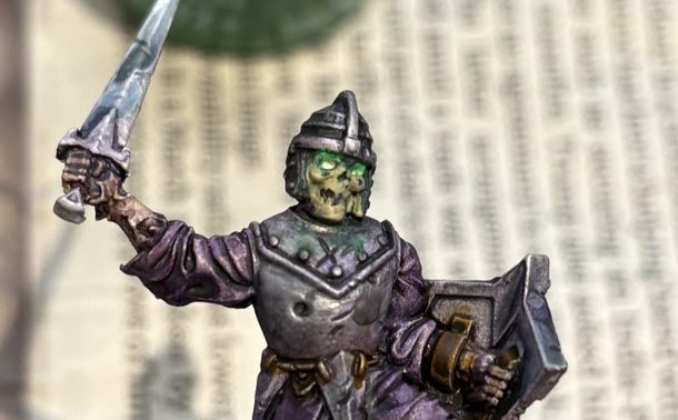 A close-up of a miniature of a skeleton, showing the skeleton’s glowing green eyes.