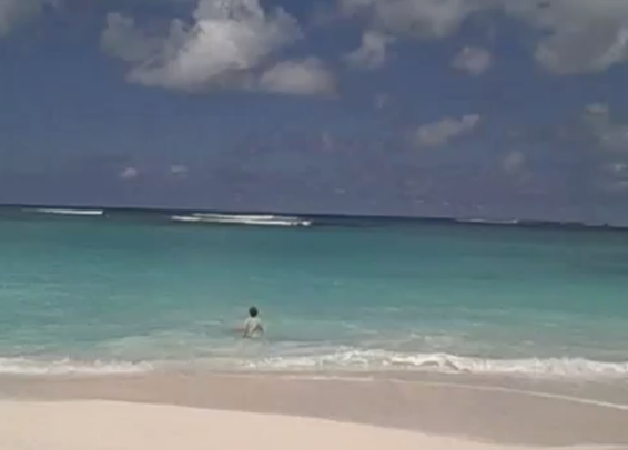 leaving a good conference: photograph of a white sand Anguilla beach with Adrian's wife swimming in blue waves