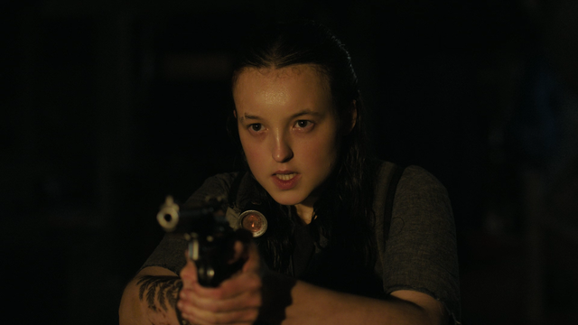 Ellie, personagem da série The Last of Us, interpretada por Bella Ramsey, aparece em um ambiente escuro com expressão intensa e determinada. Ela está com o rosto suado e os cabelos molhados, apontando uma arma com firmeza na direção da câmera. Sua postura é tensa e alerta, refletindo um momento de confronto. No braço, é possível ver uma tatuagem de folhas ou galhos. A iluminação destaca seu rosto e a arma, enquanto o fundo permanece sombreado.