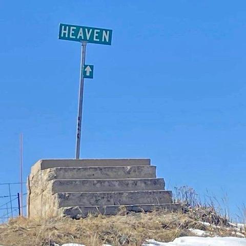 Blue sky in the background. Open space, no buildings. In the foreground there are five or so concrete stars rising to nothing on top of a splurt of unkempt brown grass. Behind the stairs is a pole with two signs: an arrow pointing up and the word Heaven.