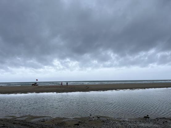 Porthtowan beach - the tide’s out, there’s a large body of shallow water trapped behind a sandbank. Lifeguards and their dinghy and van are at the edge of the water. Sky is grey, but it’s fab to be here