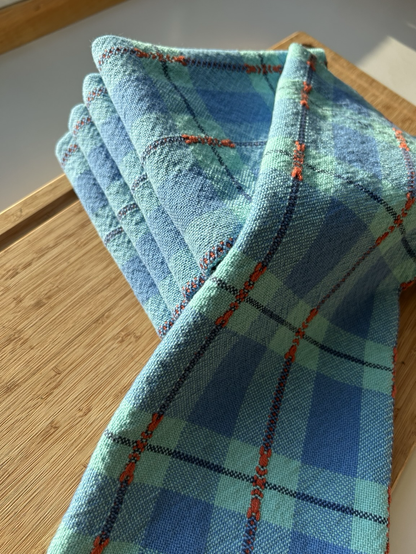 A close up look at a pile of blue checked handwoven teatowels sitting on a sunny cutting board