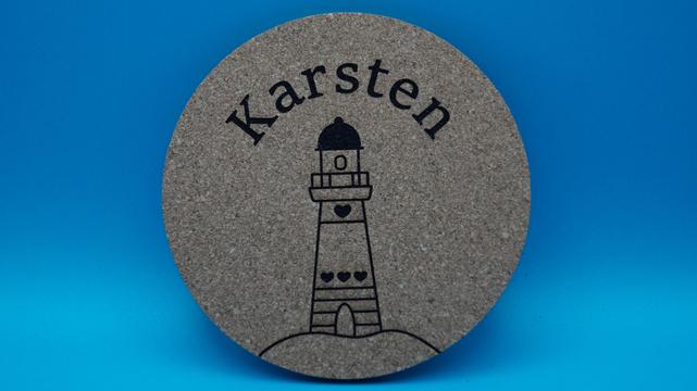 Korkuntersetzer mit Leuchtturm- und Herzmotiv, personalisiert mit dem Namen „Karsten“, als dekorative Tischkarte vor blauem Hintergrund.