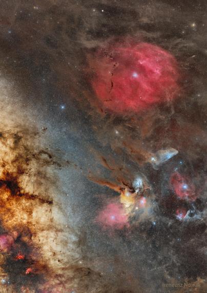 A colorful night sky image showing the Milky Way band, vibrant gas clouds, red and blue nebulas, and dense dark dust structures across a star-filled background.