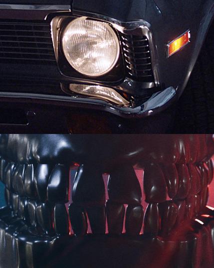 Das Bild besteht aus zwei Teilen. Oben ist ein Detailansicht der vorderen Stoßstange eines klassischen Autos zu sehen, das in dunklem Blau oder Schwarz lackiert ist. Der Scheinwerfer ist rund und hat eine glänzende, chromverchromte Umrandung. Neben dem Scheinwerfer befindet sich ein orangefarbener Blinker. Die Stoßstange hat eine horizontale Lüftung mit vertikalen Streifen. Unten ist eine stilisierte Darstellung von Zähnen in einem schwarzen, glänzenden Material zu sehen, die in einem dunklen Raum mit roter Beleuchtung platziert sind. Die Zähne sind groß und überdimensioniert, mit einer glatten Oberfläche, die an eine Skulptur erinnert.
