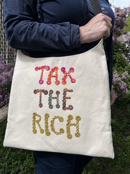 Off white canvas bag with colorful tatted lace letters on it spelling out “Tax the Rich”.