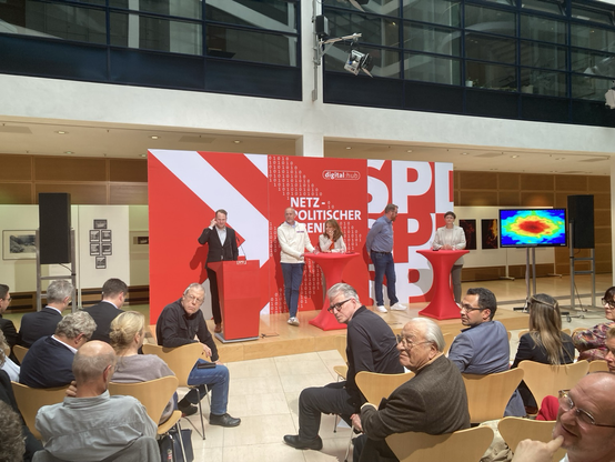 Five panelists on a stage and an audience at an event by SPD