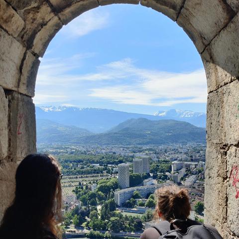 Two women watching the city of Grenoble, with mountains at the horizon 
