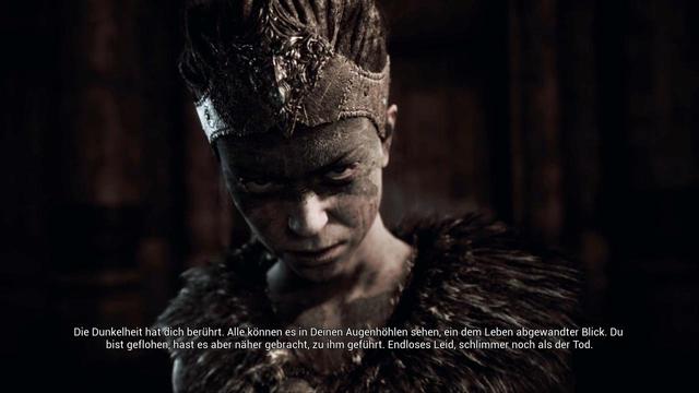 Screenshot aus dem Spiel Hellblade auf dem die Protagonistin Senua, eine junge Wikingerin zu sehen ist. Das Bild wirkt sehr düster, sie hat den Kopf leicht gesenkt und blickt direkt in die Kamera. Das Gesicht ist zum Großteil im Schatten. 

Darunter steht:
Die Dunkelheit hat dich berührt. Alle können es in Deinen Augenhöhlen sehen, ein dem Leben abgewandter Blick. Du
bist geflohen, hast es aber näher gebracht, zu ihm geführt. Endloses Leid, schlimmer noch als der Tod.