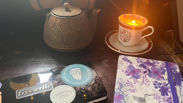A desk layout with tea, notebook, teacup-shaped candle and word processor.