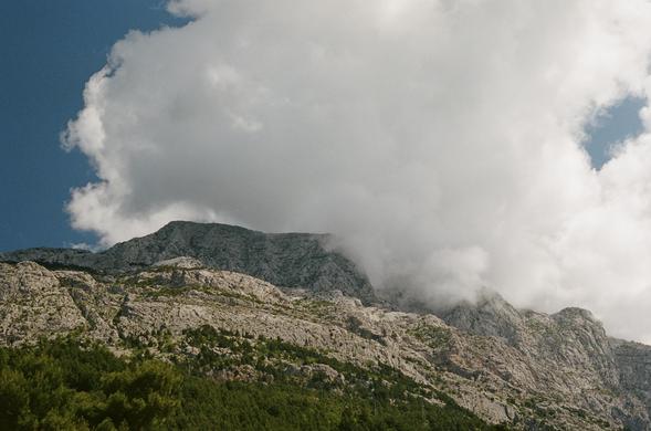 A large fluffy cloud grazing a tall mountain in front of a deep blue sky.