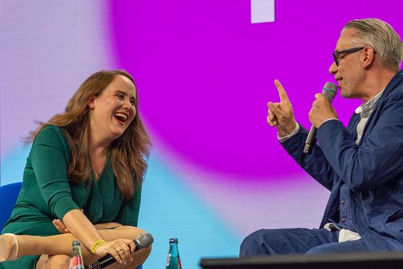 Bühne, links intensiv lachend Ricarda Lang und rechts mit erhobenem Zeigefinger und erzählend Jonny Haeusler. Beide haben Spaß.