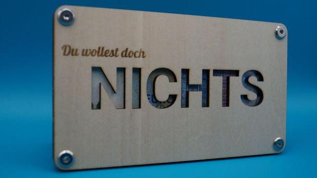 Verschraubter Holzrahmen mit der Gravur „Du wolltest doch NICHTS“, durch das Wort „NICHTS“ ist ein Geldschein sichtbar – als augenzwinkerndes Geschenk.