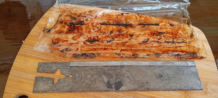 In the foreground is a rectangular saw blade. The metal is grey. Above this is cellophane stained all over with rust and some darker stained strips of deeper rust. 