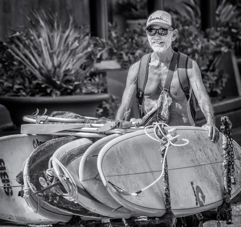 Man pushes cart of surf baords along sidewalk in front of Waikiki Beach.