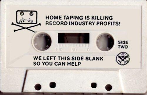 an image of a cassette tape. The label reads "HOME TAPING IS KILLING RECORD INDUSTRY PROFITS!" "WE LEFT THIS SIDE BLANK SO YOU CAN HELP"