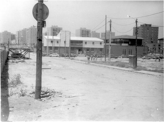 Plaza del pueblo de Orcasur años 1960 o 70. Se ve una calle sin asfaltar con postes de la luz con cables, farolas y al fondo edificios de viviendas