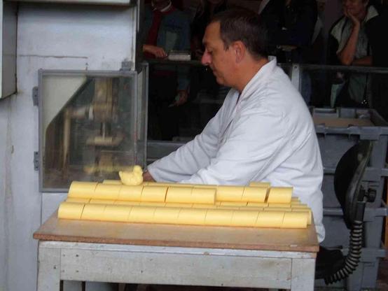 Person in a white shirt working at a table, arranging cut, light yellow soap bars, into the shape of a duck.