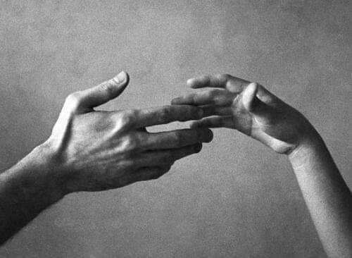 Black & white picture of two hands gently, tentatively touching.