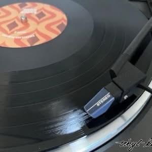 Nahaufnahme einer Schallplatte, die auf einem Plattenspieler abgespielt wird, mit einem bunten Etikett und einer Nadel, die über die Rillen der Platte gelegt wird.