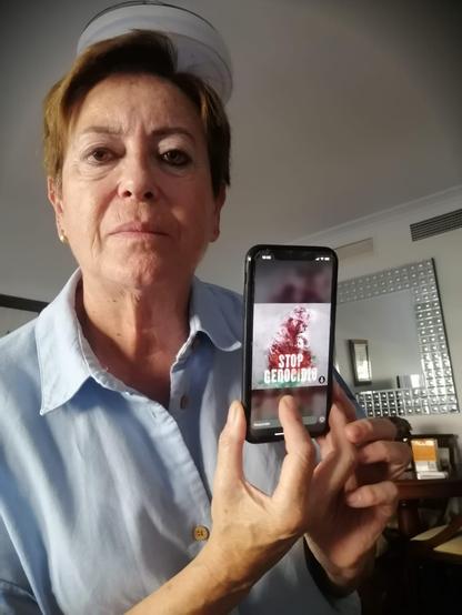 Una mujer sosteniendo un smartphone en el que se ve una imagen con el lema "STOP GENOCIDIO"