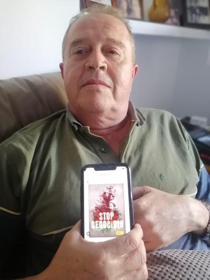 Un hombre sosteniendo un smartphone en el que se ve un cartel con el lema STOP GENOCIDIO.