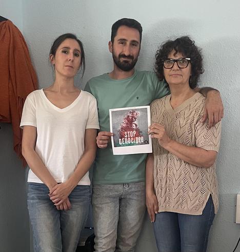 Dos mujeres y un hombre sosteniendo un cartel con el lema STOP GENOCIDIO.