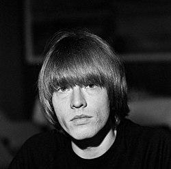 Brian Jones, con su característico pelado a cazoleta, en una fotografía promocional de Olavi Kaskisuo / Lehtikuva, cerca de 1965, donde nos mira serio y con marcadas ojeras en un rostro avejentado para sus 23 años. Dominio público.
