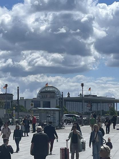 Foto mit Blick auf den Reichstag. Leicht bewölkter Himmel, Menschen im Vordergrund.
