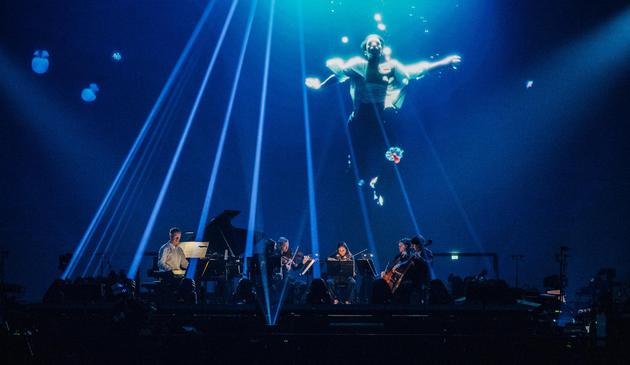 Max Richter au piano accompagné de ses 5 musiciens aux cordes, devant une vidéo projetée les surplombant, où l’on voit un danseur nageant sous l’eau