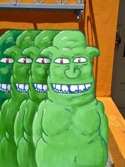 A drawing of four orks standing in a line. They are all green with big toothy smiles. An orange wall is behind them. 