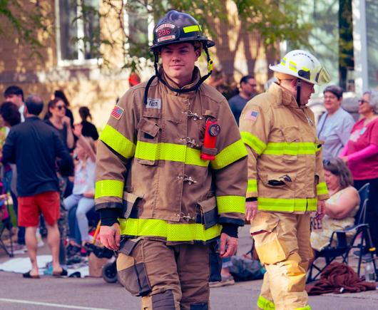 A firefighter in the middle of the frame is looking roughly in my direction while one behind him looks the other way with a crowd of bystanders behind