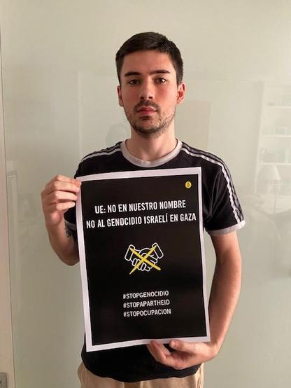 Un joven sosteniendo un cartel con el texto UE: NO EN NUESTRO NOMBRE 
NO AL GENOCIDIO ISRAEL EN GAZA 
#STOPGENOCIDIO
#STOPAPARTHED
#STOPOCUPACION