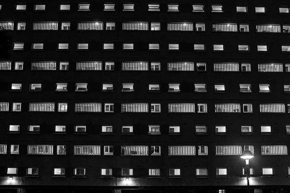 Schwarzweissfotografie einer Hausfront mit vielen Fenstern in der Nacht. 
