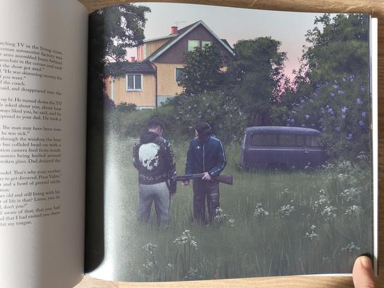 An illustration from "Swedish Machines: Sunset at Zero Point" by Simon Stålenhag showing a couple of armed teen-agers in long grass infront of a house in rural Sweden.