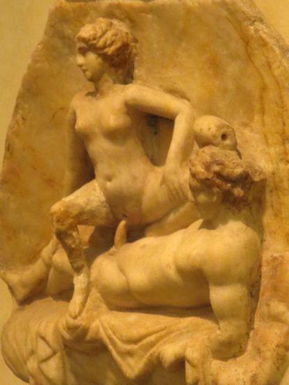 Relief of a woman riding an erect phallus. The man is lying down, propped up on one elbow, the other arm draped over his head. She is crouching, possibly about to get off or just in the act of going up and down. She is facing away from him while he looks at her vulva or at his own phallus. Both are naked.
