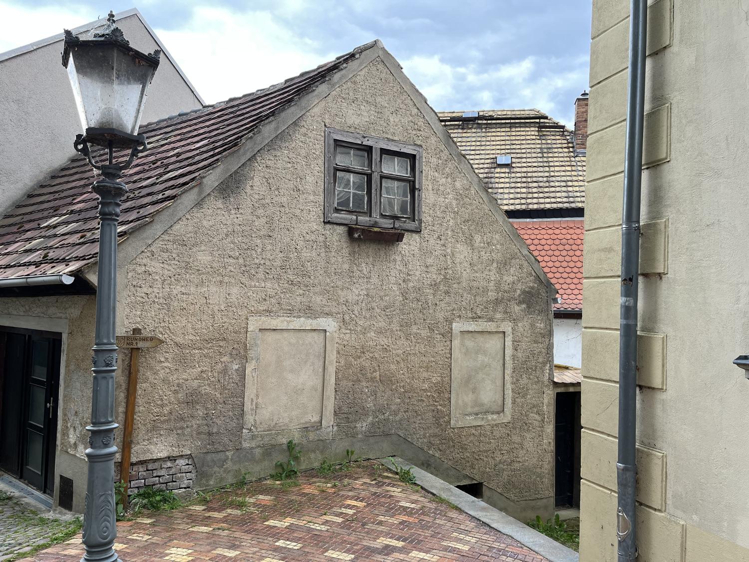 Fassade mit zwei zugemauerten Fenstern im Erdgeschoß und einem Doppelfenster im Dachgeschoß