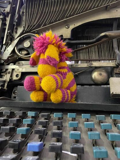 yellow and pink knitted zebra sitting on a Linotype typesetting machine
