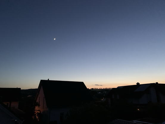 Dee Mond leuchtet am orange-blauen Abendhimmel vor schwarzem Horizont 