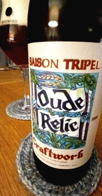 Close-up of a bottle of Oude Relic craft beer by Craftwork. Glass with freshly poured beer in the background.