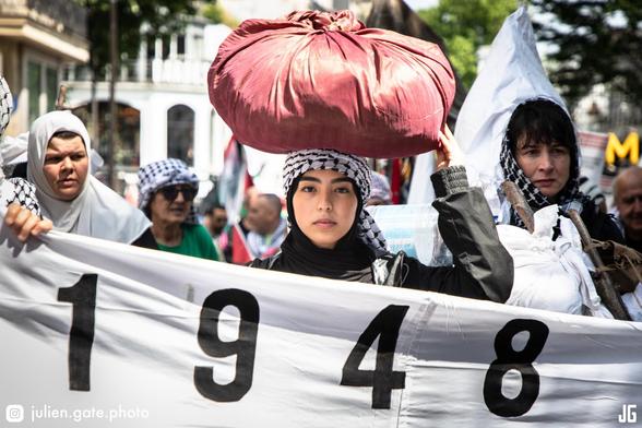 Cette photo a été prise boulevard Marguerite de Rochechouart, peu après le croisement avec le boulevard de Magenta. On y voit des manifestantes portant des baluchons sur leurs têtes, tenant une banderole sur laquelle est inscrit « 1948 ». Cette scène évoque l’exode forcé des Palestiniens lors de la Nakba.