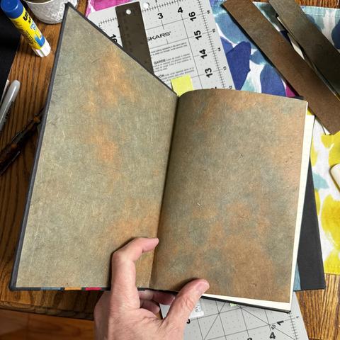 Interior of a handmade book. Endpaper that’s sort of a mottled greenish brown. 