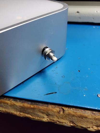 Closeup of the silver side of a 2008/2009 Mac Mini. A button with some kind of threaded enclosure is loosely hanging out of a circular hole in the metal chassis.