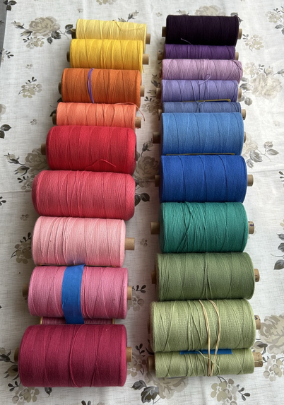 Two rows of spools of coloured weaving yarn in a rainbow of colours