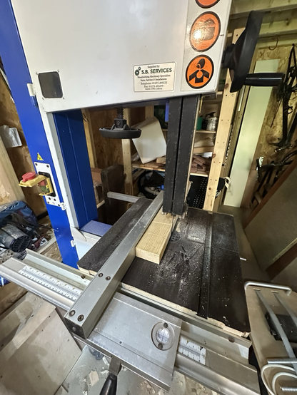 A bandsaw cutting small plank along it’s length