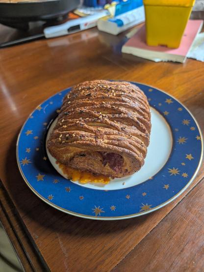 croissant with everything bagel sprinkles on top, cheese melted out the front on a blue rimmed plate