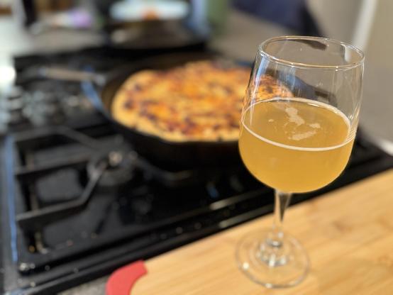 A glass of Dressler Estate's Valley Creek Blend cider with a Chicago-style deep dish pizza in the background.