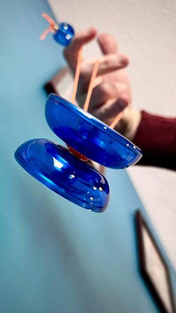 Shot from underneath, a clear blue Hyper Freehand yo-yo by Duncan/Bandai. The yo-yo is set up for 5A (Freehand) play with a clear blue die counterweight. A blue wall and white ceiling split the background diagonally. 