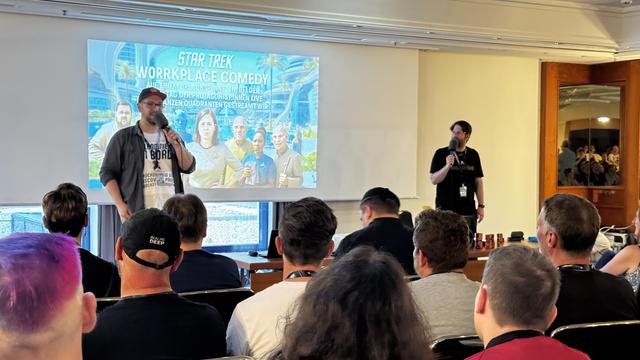 Two speakers present a session titled "Star Trek Workplace Comedy" at an event, with an audience visible in the foreground. A screen in the background displays the session title along with images related to Star Trek.