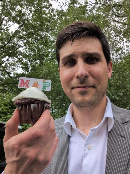 Devin holding a cupcake with the MAP Family Learning Center logo on it.